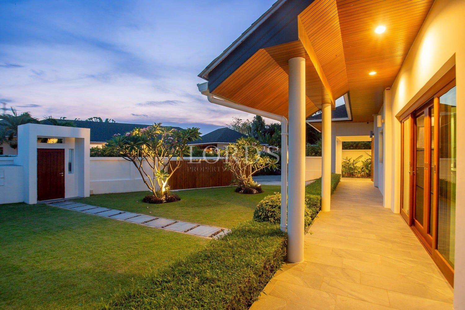Modern villa exterior with covered walkway, landscaped garden, and evening lighting