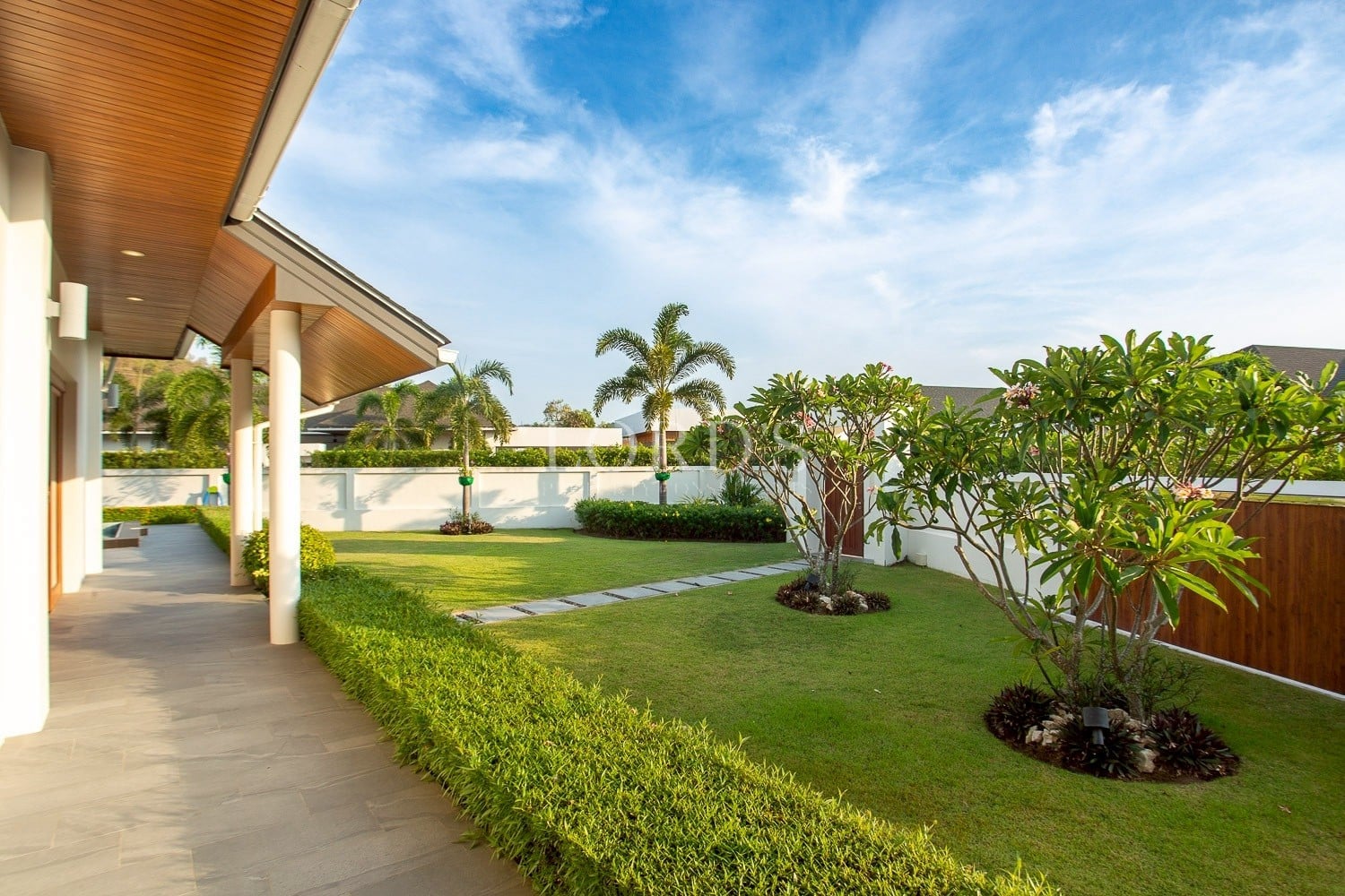 Landscaped villa garden with green lawn, palm trees, and covered walkway