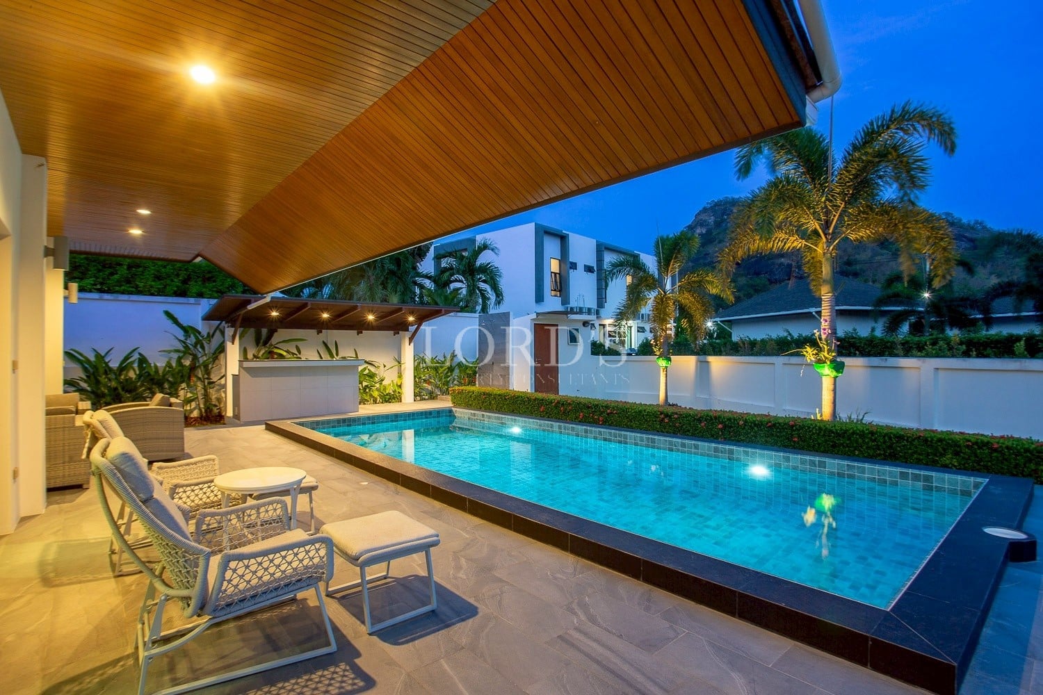 Luxury villa pool at night with covered patio, outdoor seating, and ambient lighting