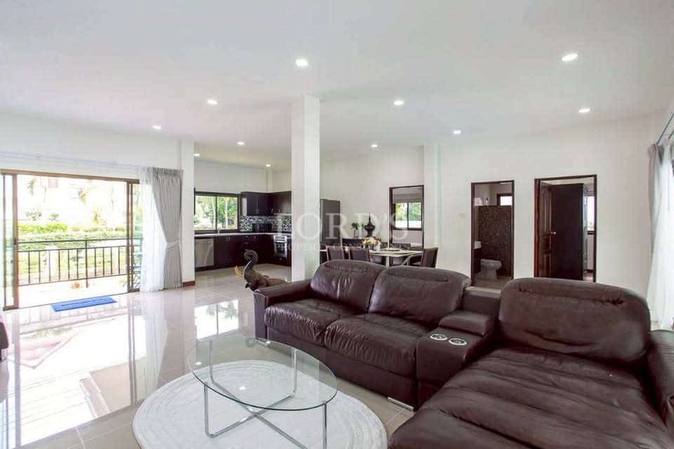 Spacious open-plan living room with leather sofa, glass coffee table, glossy tiled floor, and kitchen in the background