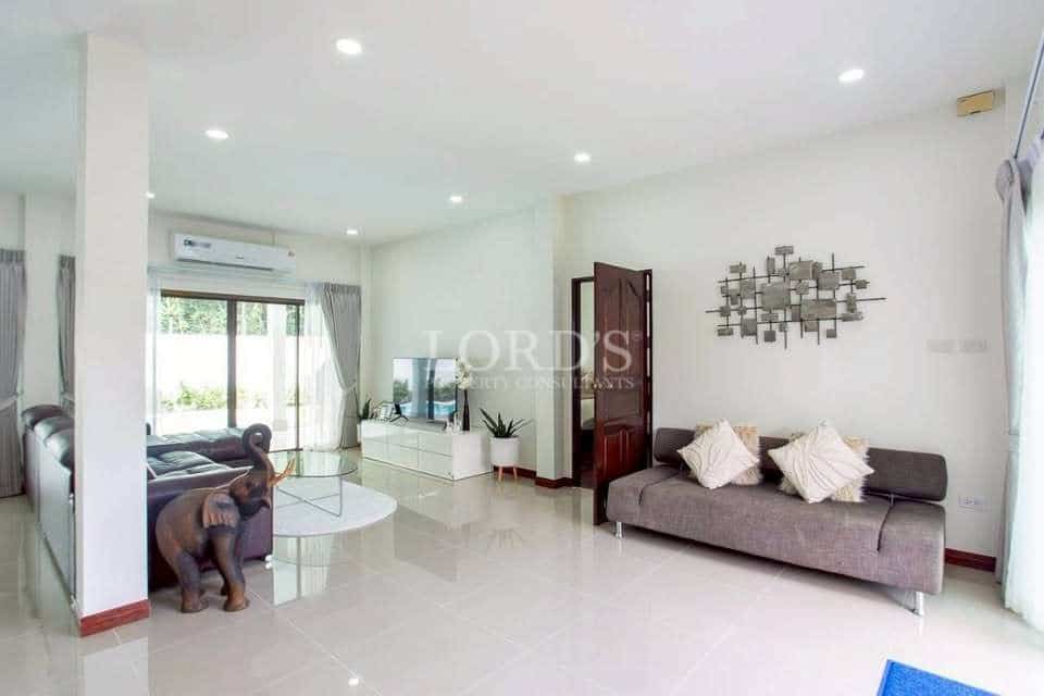 Modern living room with minimalist furniture, glossy tiled floor, wall-mounted TV, large windows, and natural light