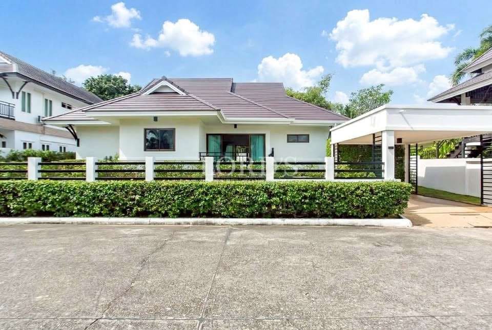 Modern single-story house with gated fence, covered carport, manicured hedge, and tiled roof under a blue sky