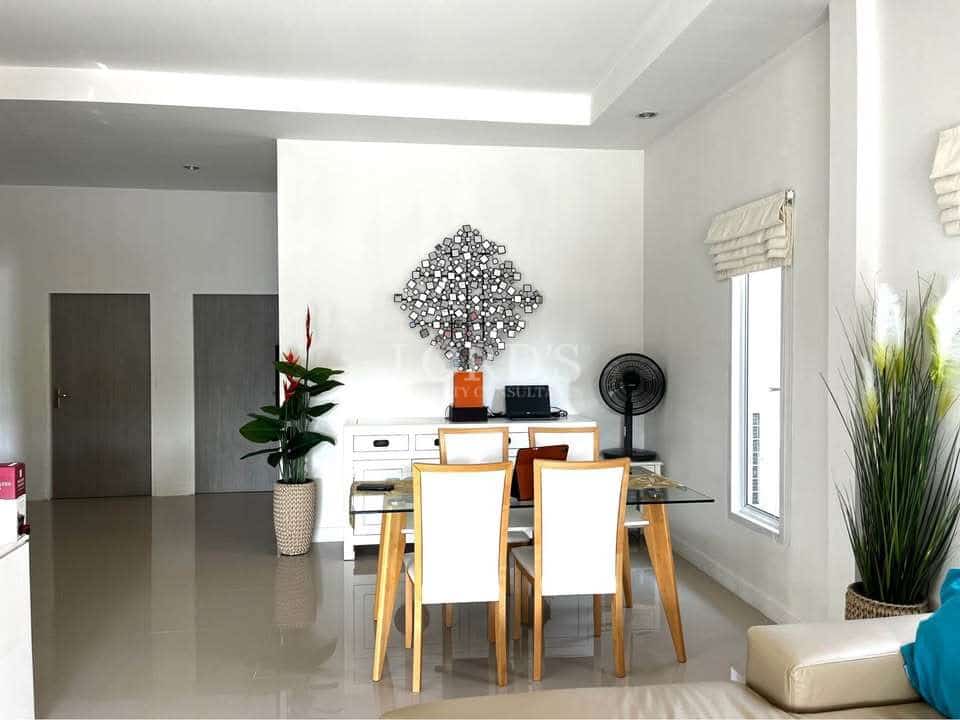 Modern dining area with glass table, wooden chairs, decorative wall art, glossy tiled floor, and natural light