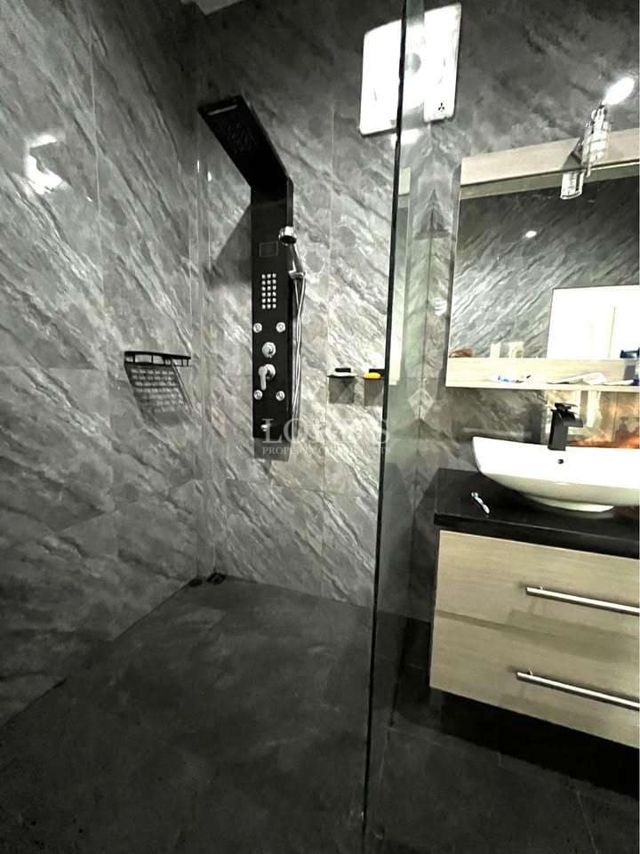 Modern walk-in shower with glass enclosure, rainfall shower panel, dark marble tiles, and floating vanity