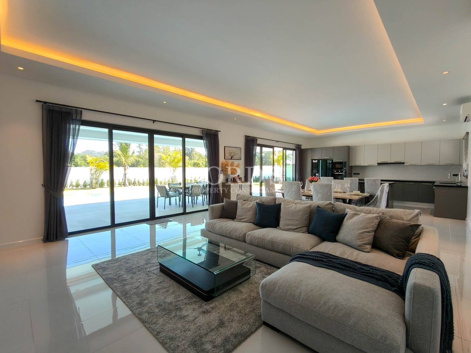 Spacious open-plan living room with ambient ceiling lighting, sectional sofa, sliding glass doors, and pool view.Spacious open-plan living room with ambient ceiling lighting, sectional sofa, sliding glass doors, and pool view.