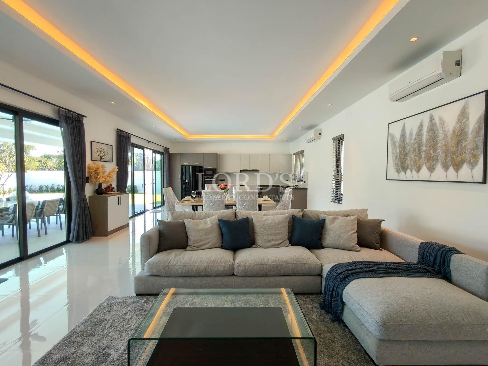 Modern open-plan living room with ambient ceiling lighting, sectional sofa, and dining area in the background.