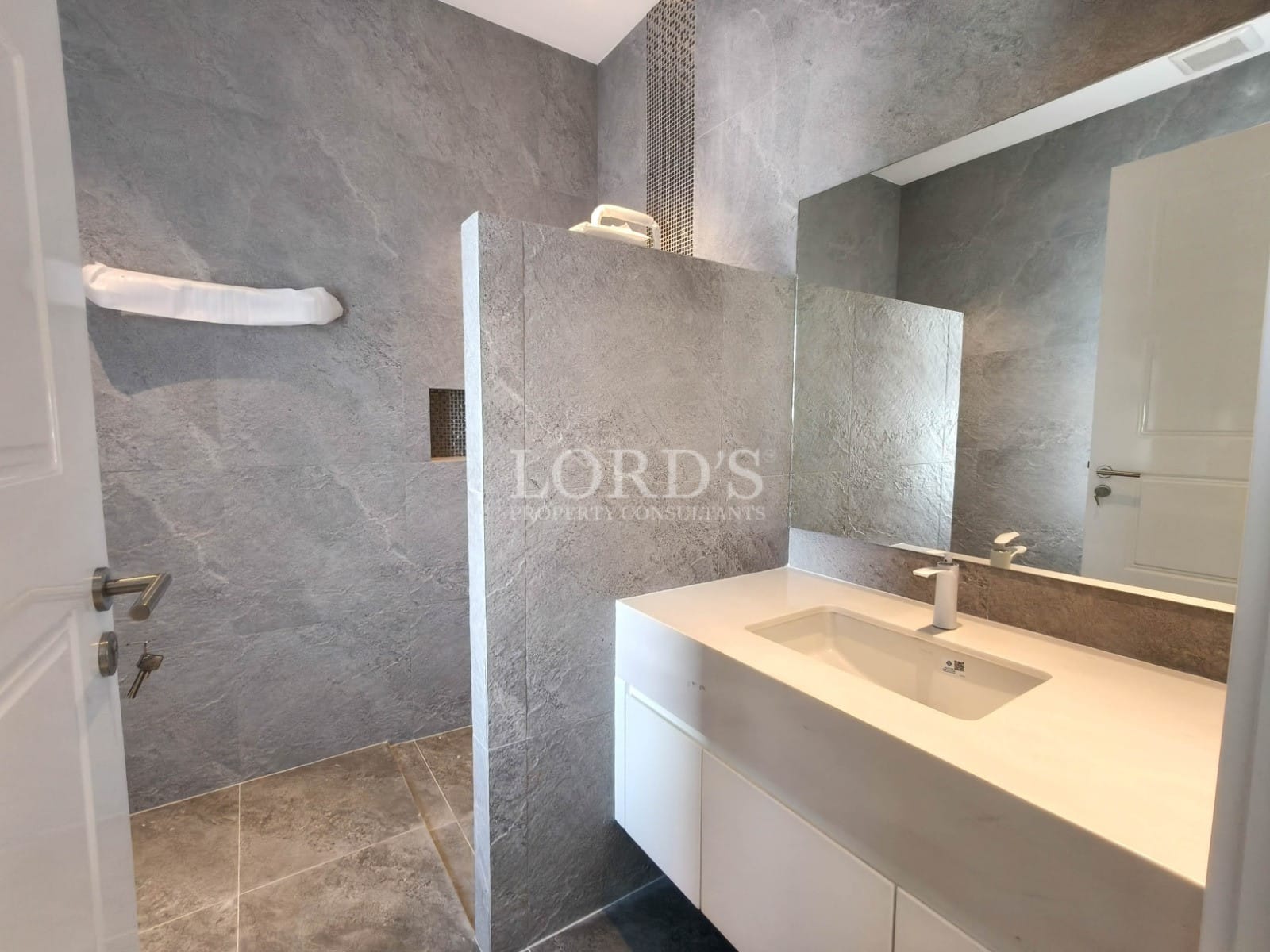 Modern bathroom with walk-in shower, floating vanity, stone-look tiles, and large mirror.