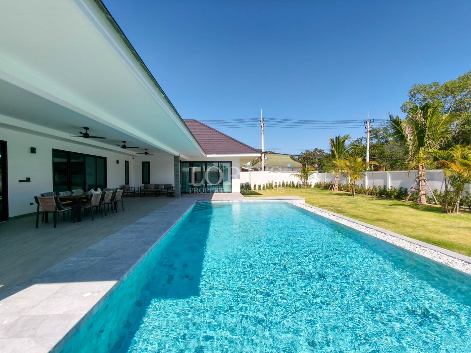 Large private swimming pool with covered outdoor dining area, landscaped garden, and modern villa design.