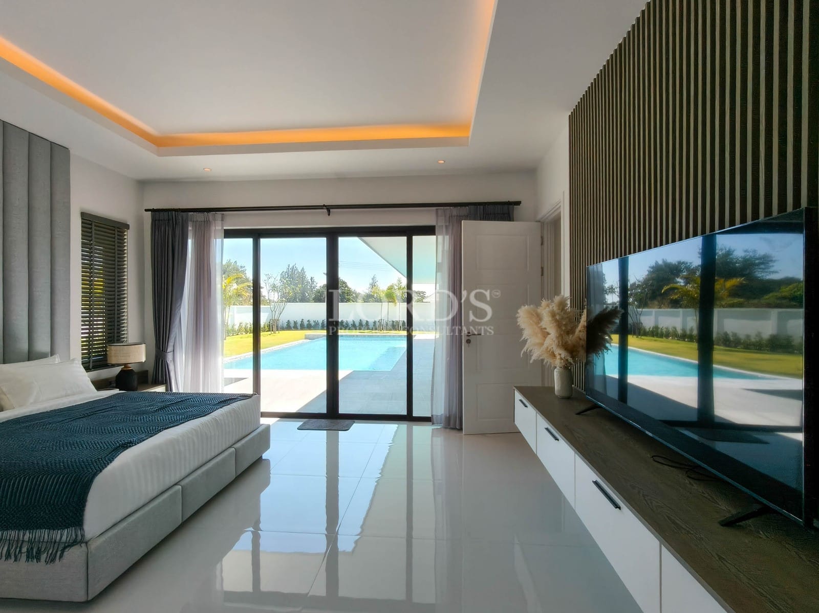 Modern bedroom with pool access, wall-mounted TV, ambient ceiling lighting, and sliding glass doors.