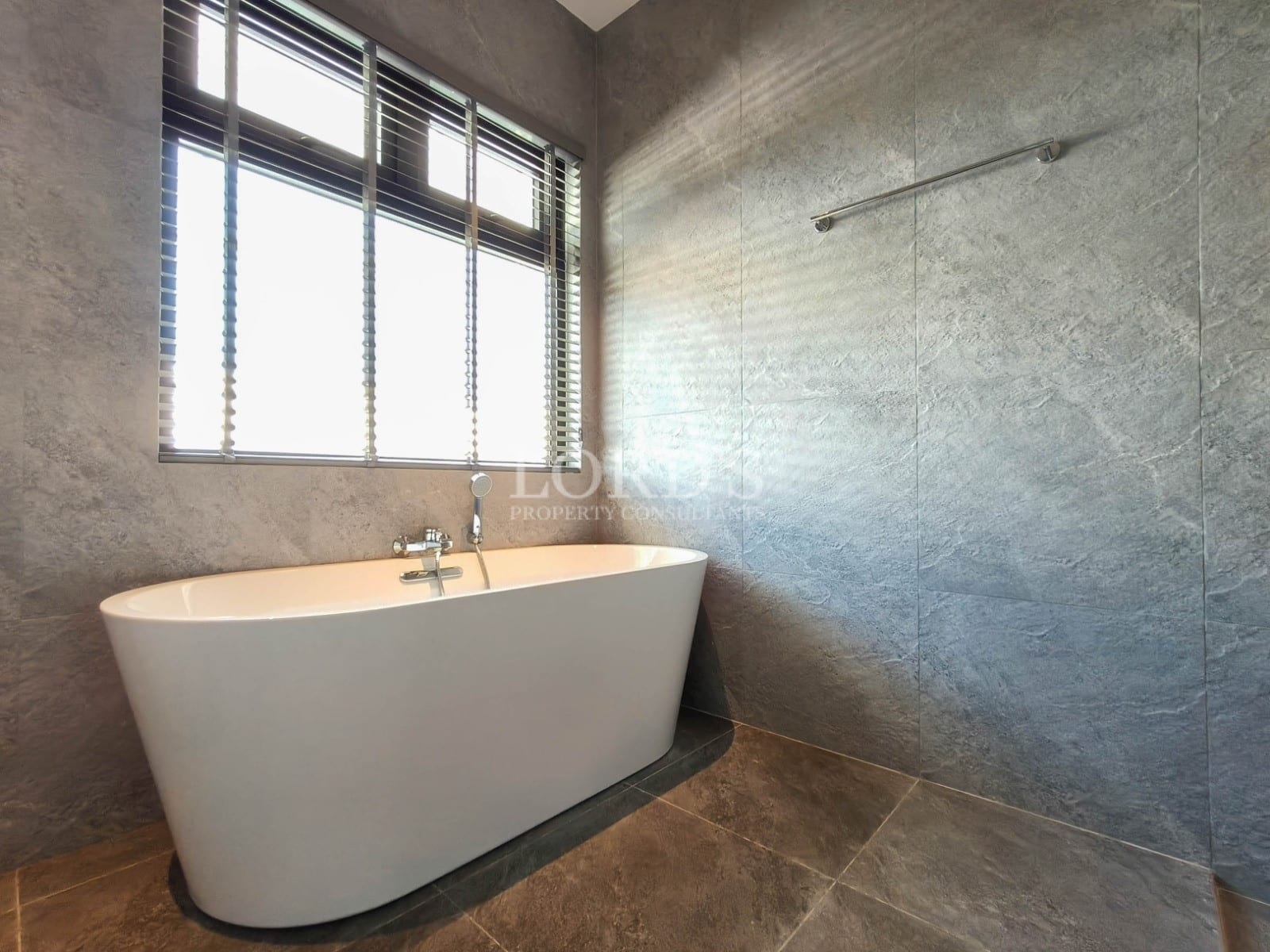 Modern bathroom with freestanding bathtub, textured tile walls, and large window for natural light.