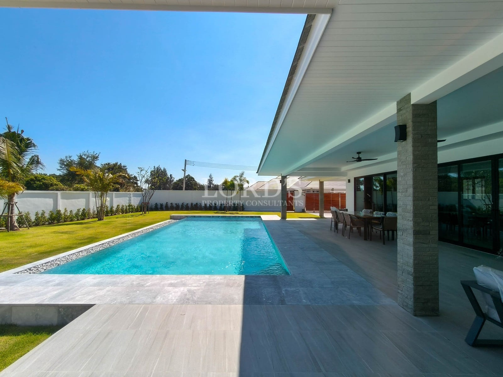 Modern private swimming pool with covered outdoor dining terrace and landscaped garden.
