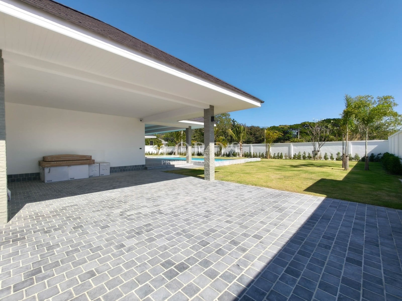 Covered outdoor terrace with tiled flooring, landscaped garden, and modern villa structure.