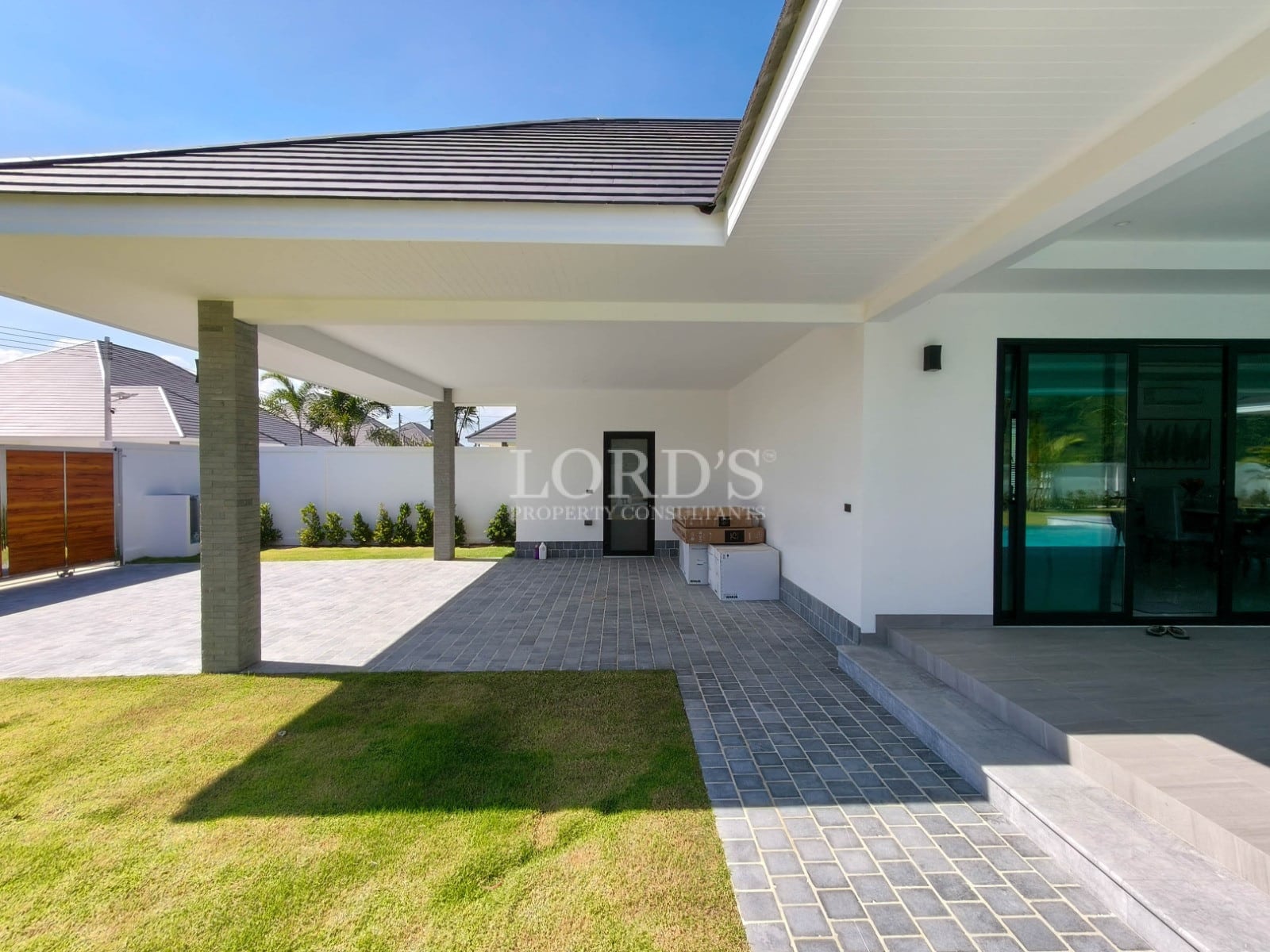 Covered carport and entrance area with tiled driveway, landscaped garden, and modern villa exterior.