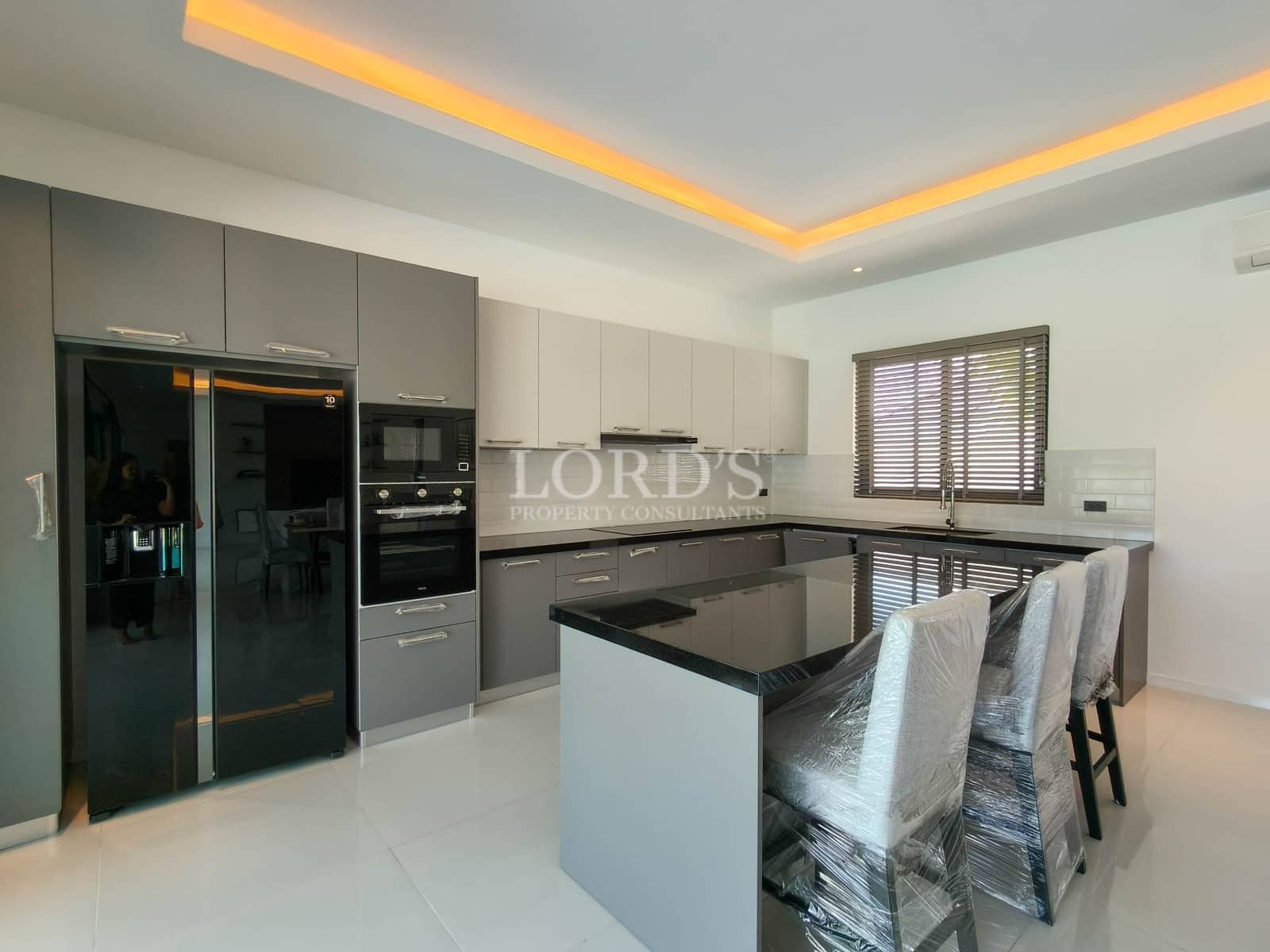 Modern villa kitchen with central island, breakfast bar seating, built-in appliances, and ambient ceiling lighting.