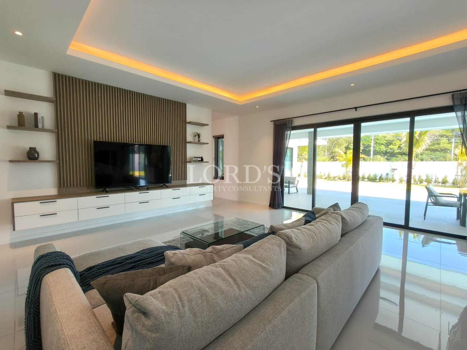 Modern living room with feature TV wall, ambient ceiling lighting, sectional sofa, and sliding glass doors to the terrace.