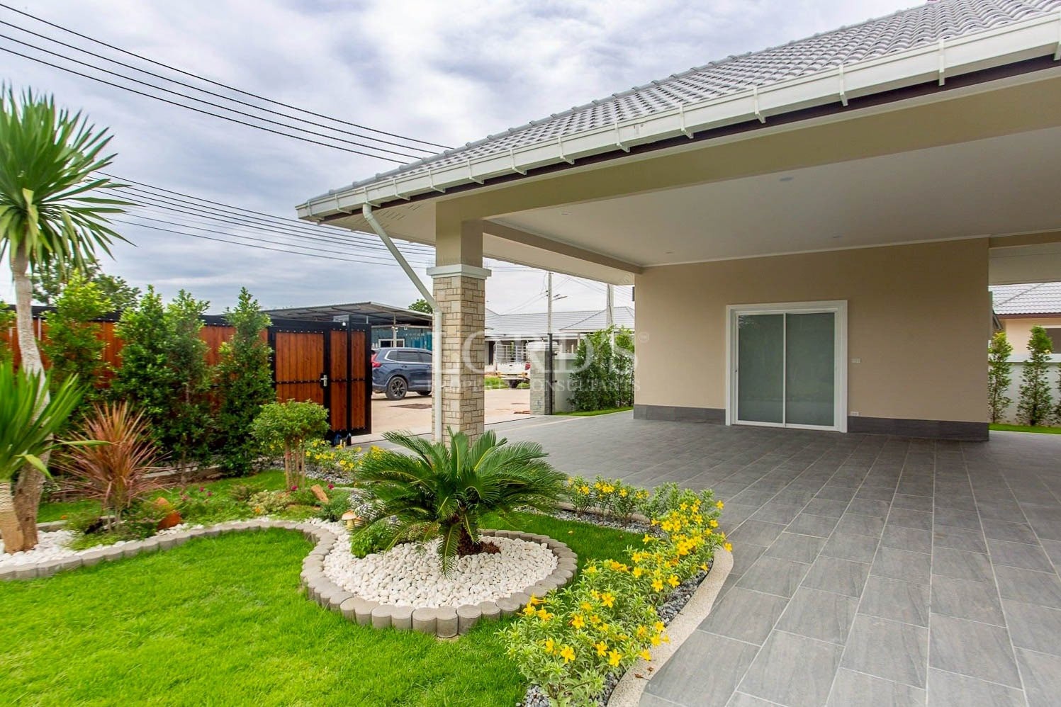 Modern single-storey house with covered carport, landscaped tropical garden, and tiled driveway.