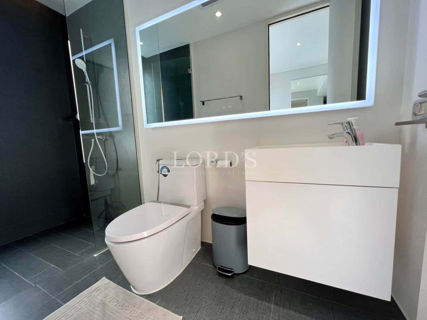 Modern minimalist bathroom with a glass walk-in shower, wall-hung vanity, illuminated mirror, and sleek white toilet.