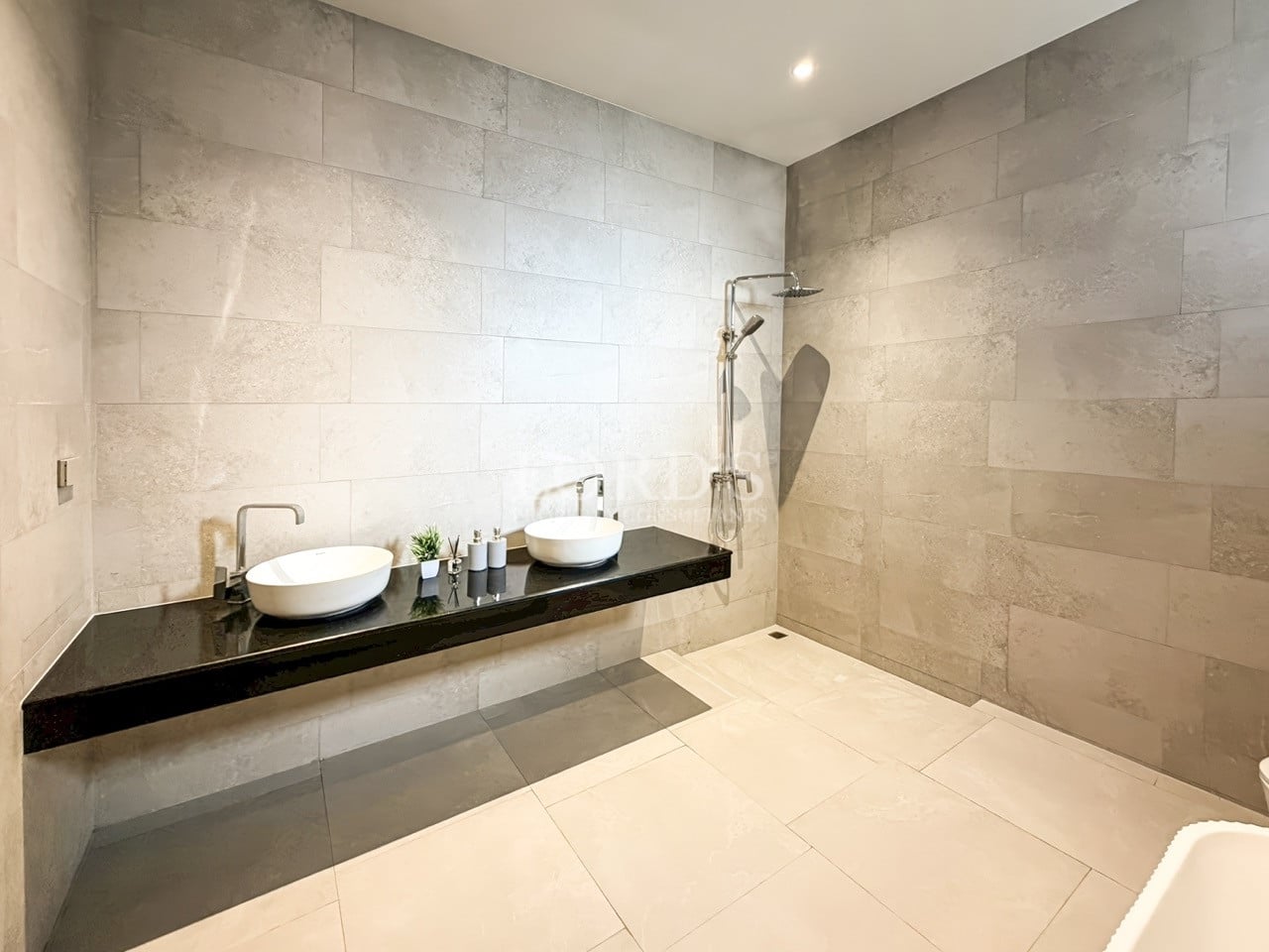 Modern walk-in bathroom with double vessel sinks, floating black vanity, stone tile walls, and open rain shower.