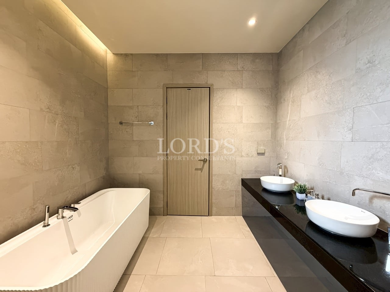 Modern bathroom with freestanding bathtub, double vessel sinks, stone tile walls, and minimalist vanity.
