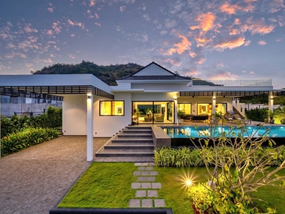 Luxury modern villa exterior at dusk with illuminated swimming pool, landscaped garden, and covered terraces