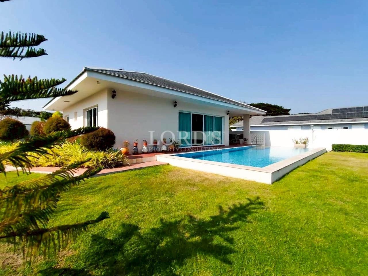 Modern single-story villa with private swimming pool, green lawn, and outdoor patio.