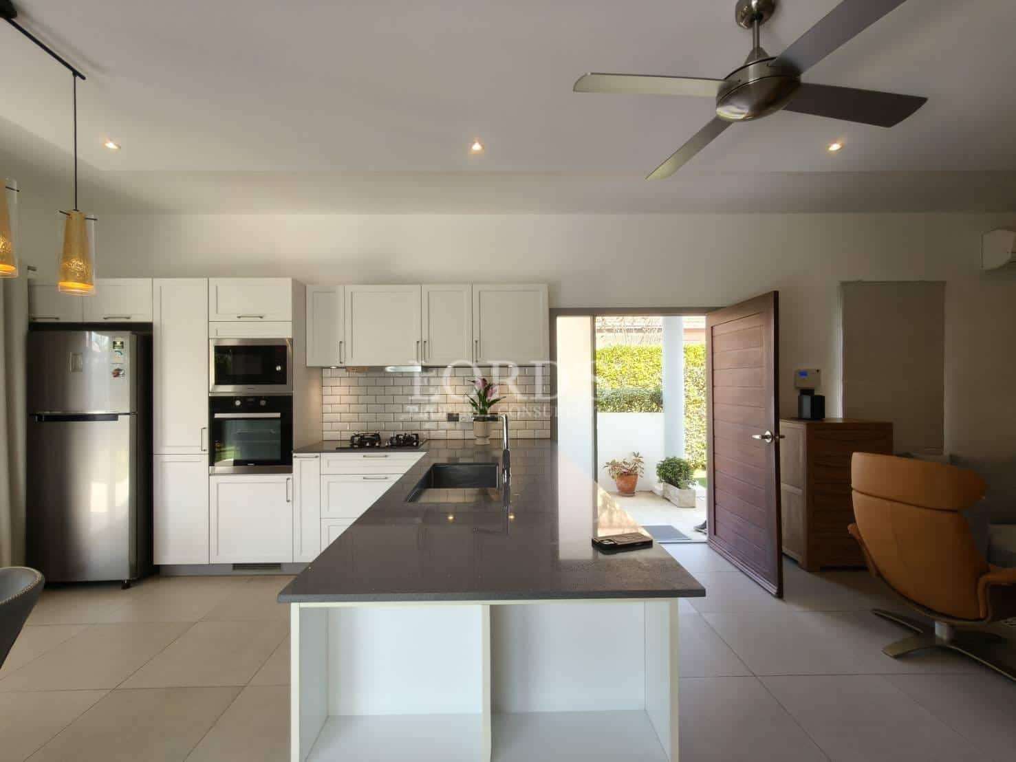 Modern open kitchen with white cabinetry, central island, built-in appliances, pendant lighting, and natural light from patio doors.