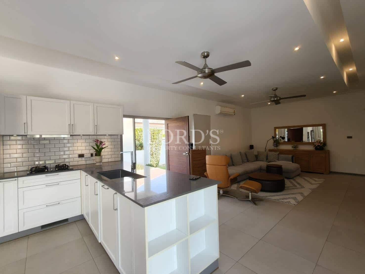 Open-plan modern kitchen and living area with white cabinetry, kitchen island, ceiling fans, and contemporary furniture.