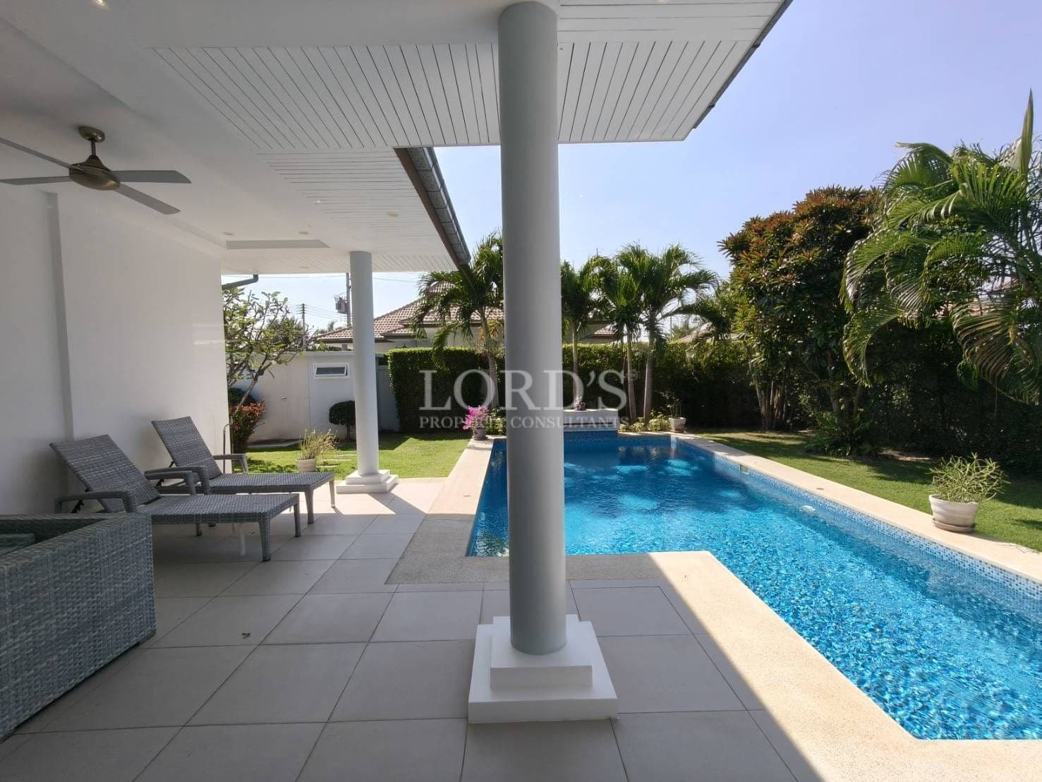 Private pool terrace with covered patio, sun loungers, modern columns, and landscaped tropical garden.