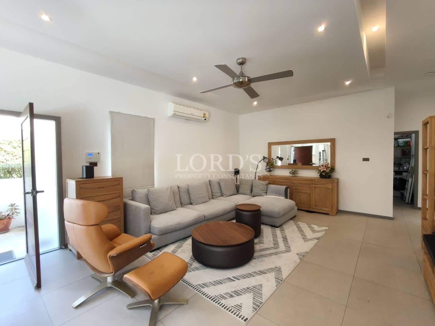 Spacious modern living room with sectional sofa, leather lounge chair, ceiling fan, air conditioning, and recessed lighting.