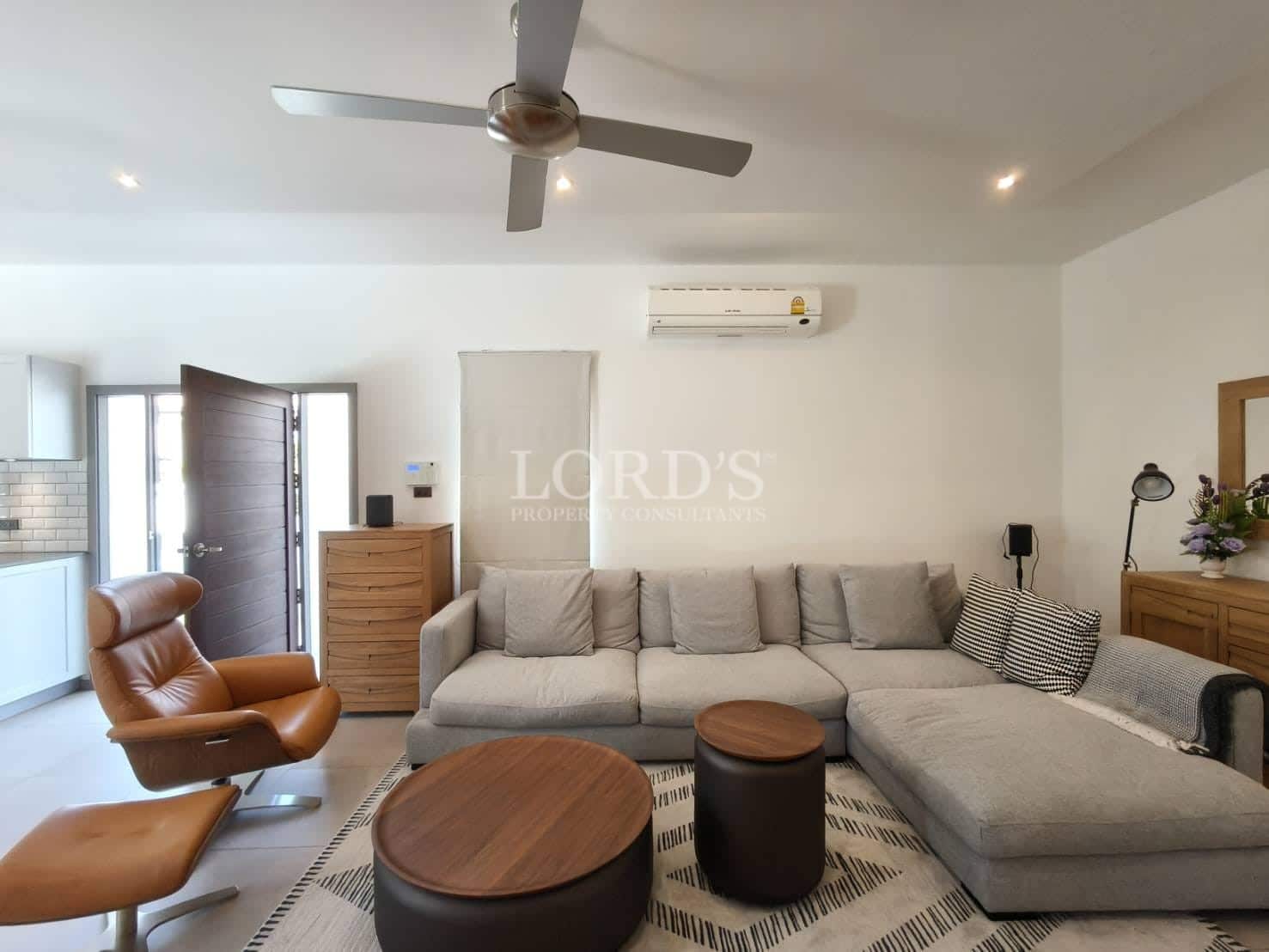 Modern living room with sectional sofa, leather lounge chair, ceiling fan, air conditioning, and open-plan layout.