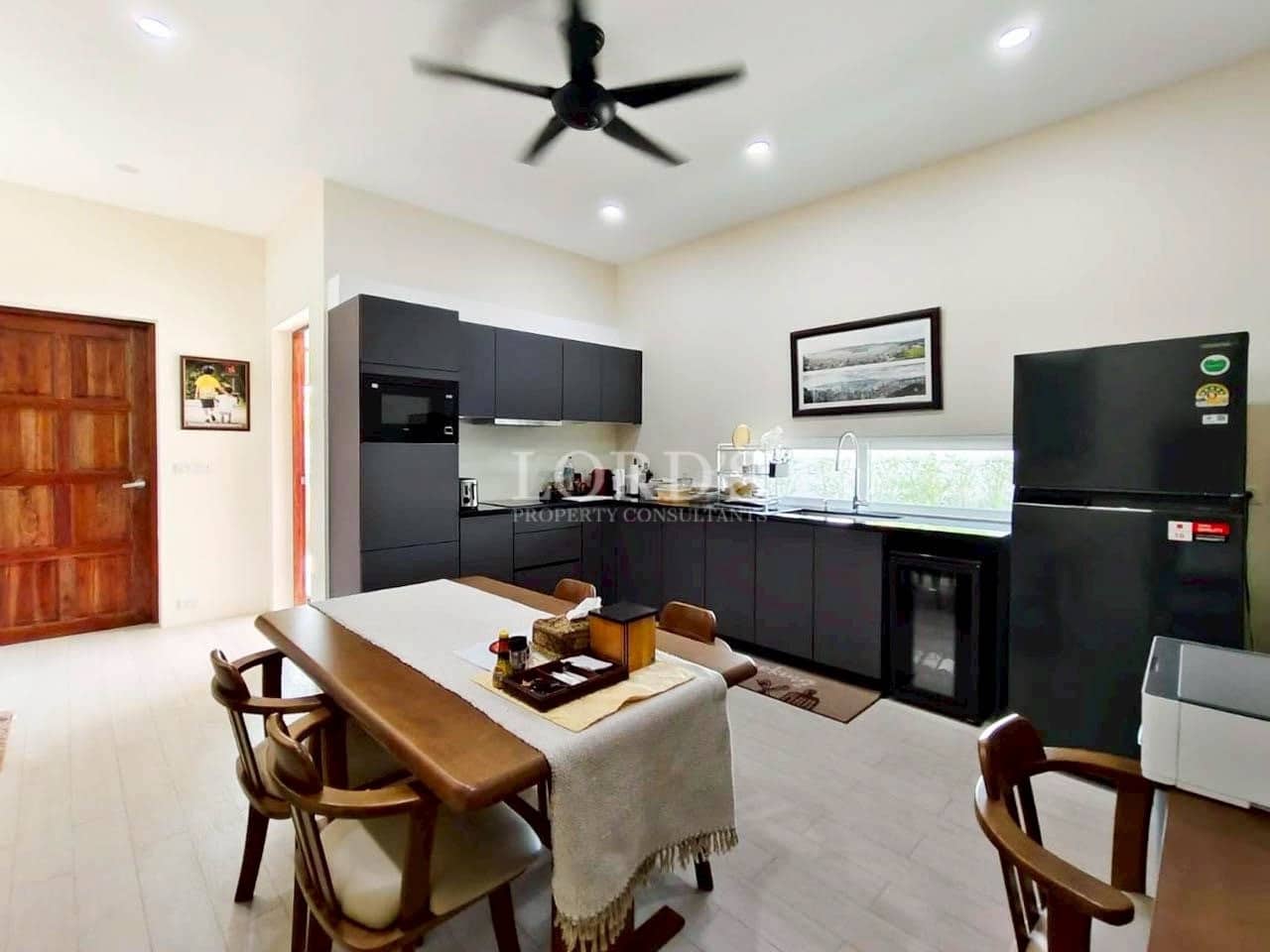 Modern open-plan kitchen with matte black cabinets, dining table, ceiling fan, and built-in appliances.