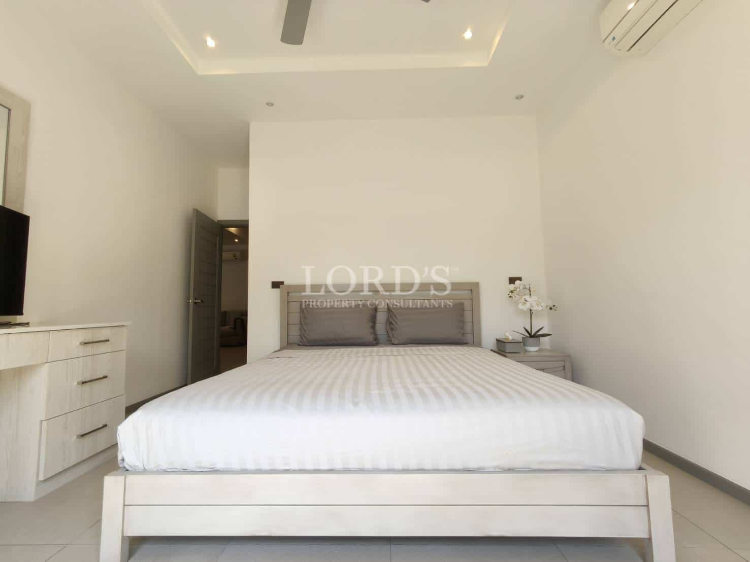 Bright modern bedroom with double bed, minimalist furniture, ceiling fan, air conditioning, and soft recessed lighting.