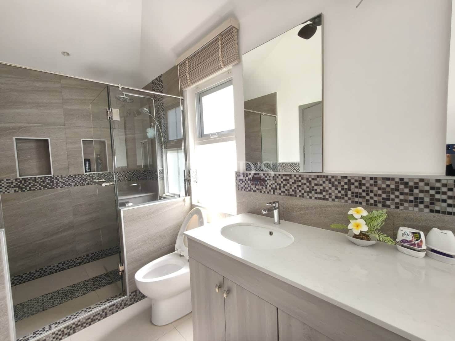 Modern bathroom with glass-enclosed shower, mosaic tile accents, vanity sink, large mirror, and natural light from a window.