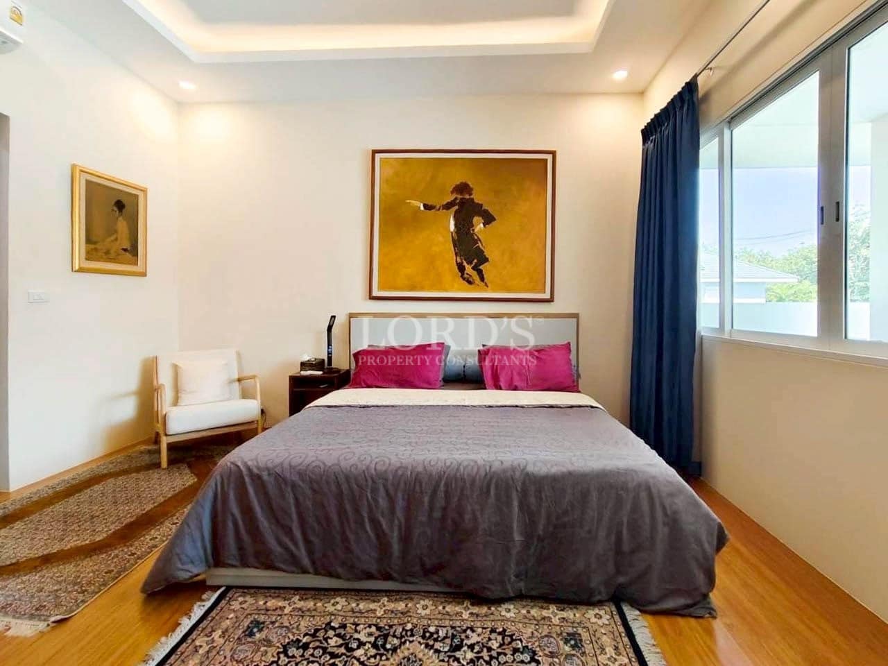 Modern bedroom with wooden flooring, large window, framed wall art, and minimalist decor.