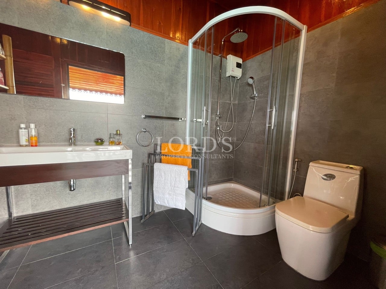 Modern bathroom with glass shower enclosure, rain shower, vanity sink, gray tiles, and toilet.