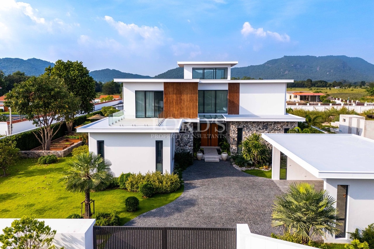 Front exterior view of a modern luxury villa with stone façade, wood accents, and landscaped driveway.
