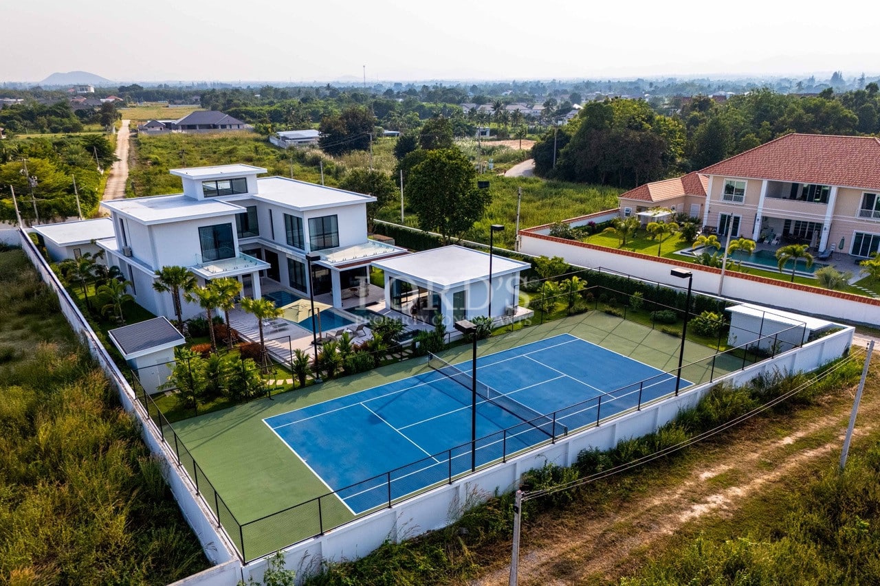 Aerial view of a modern luxury villa with private swimming pool, landscaped garden, and full-size tennis court.