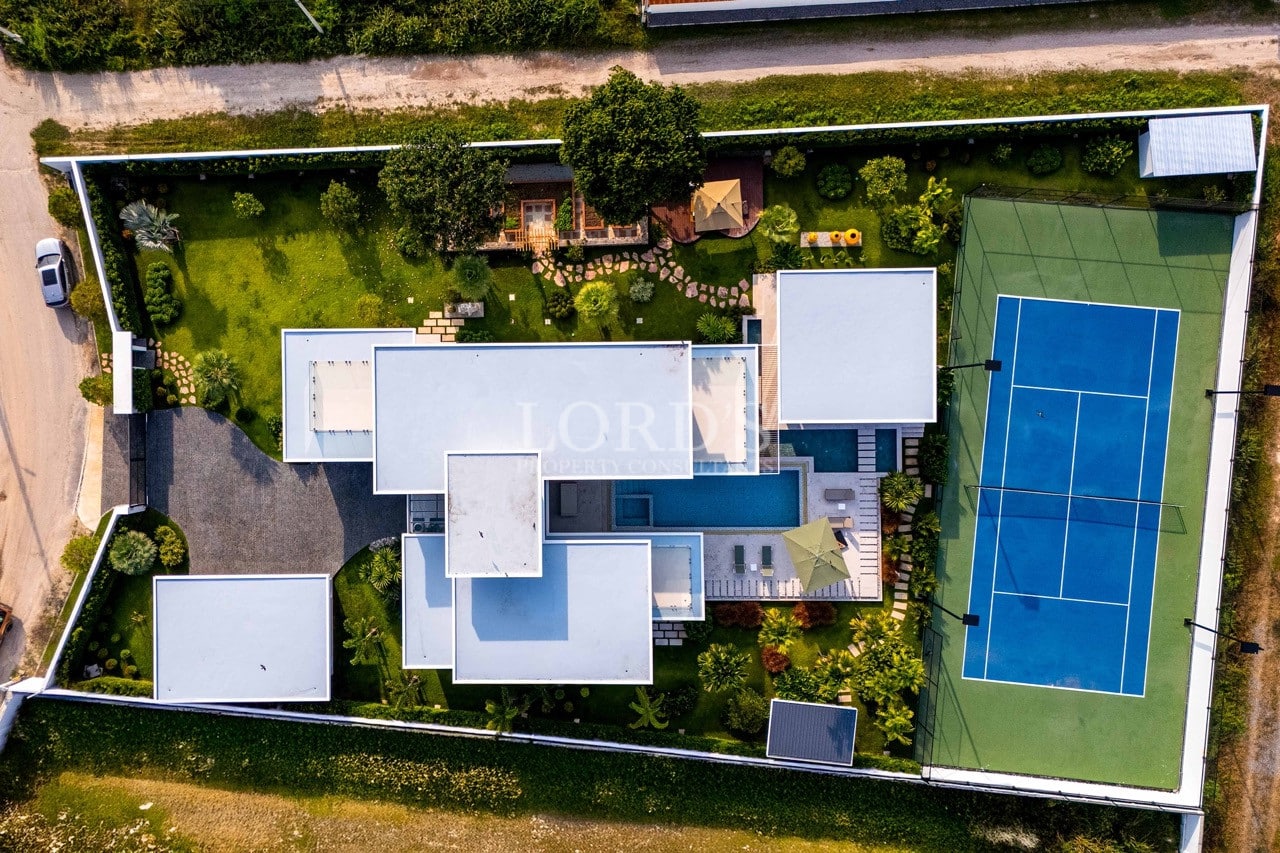 Top-down aerial view of a modern luxury villa with swimming pool, landscaped garden, and private tennis court.