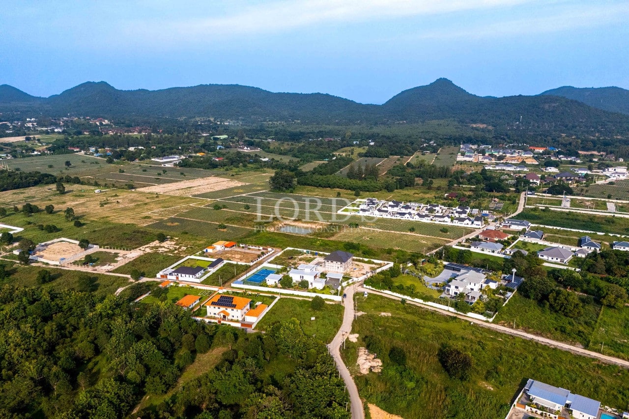 Aerial view of residential development surrounded by green fields and mountains under a clear blue sky.