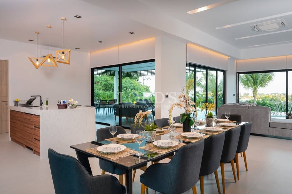 Elegant open-plan dining and kitchen area with modern island, designer pendant lights, and garden-facing glass doors