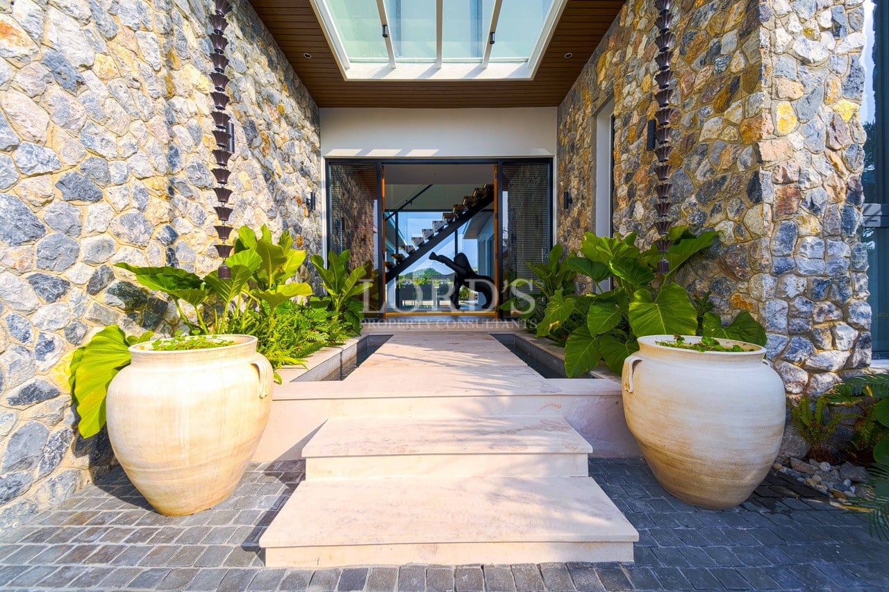Luxury villa entrance with stone walls, landscaped walkway, and skylight feature.