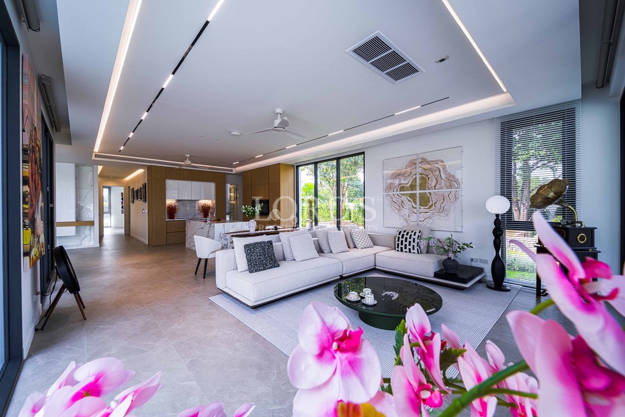 Spacious modern living room with an open-plan layout, featuring a sectional sofa, designer lighting, floor-to-ceiling windows, and seamless connection to the kitchen and dining area.