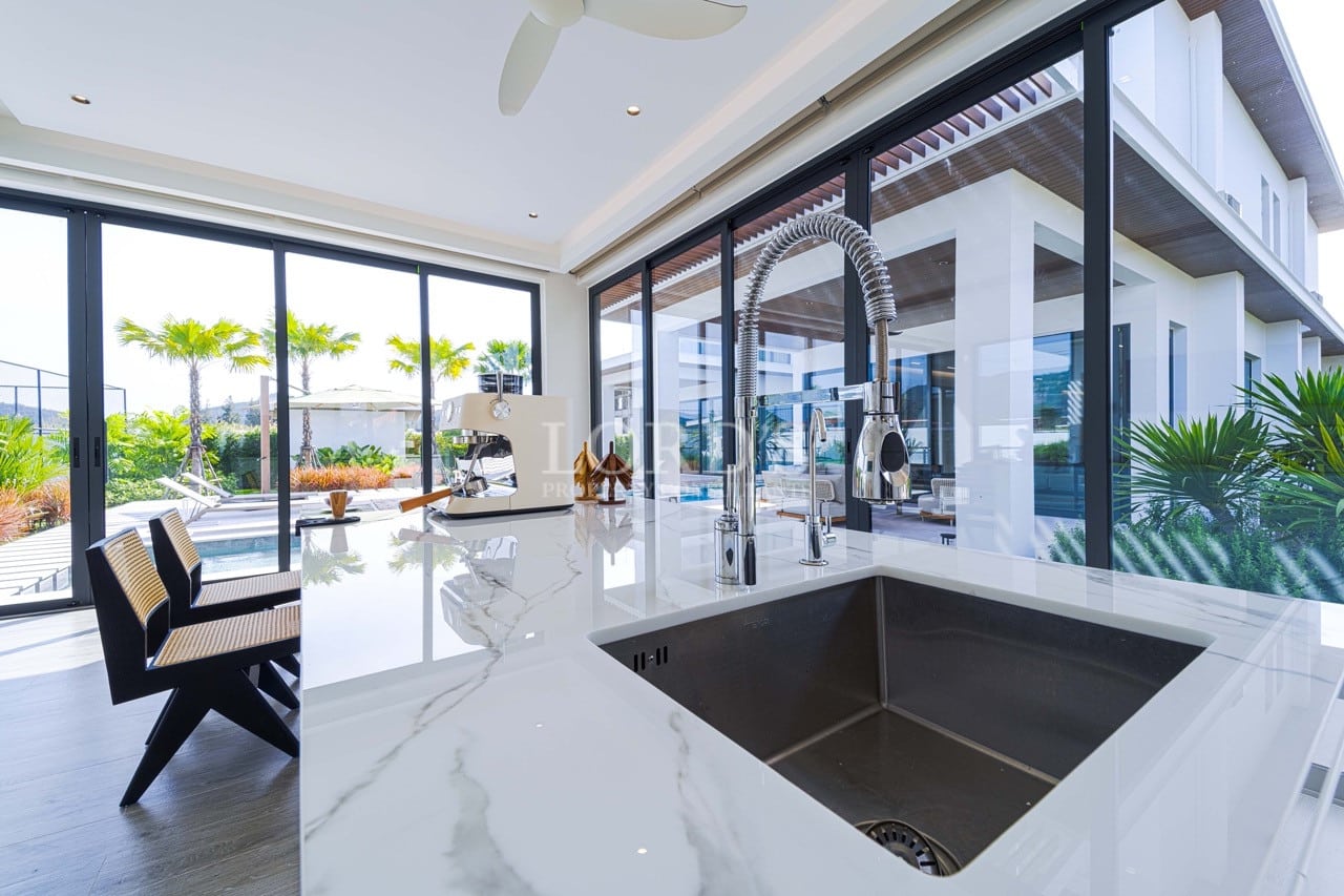 Modern kitchen island with marble countertop, stainless steel sink, and large glass doors opening to an outdoor pool area.