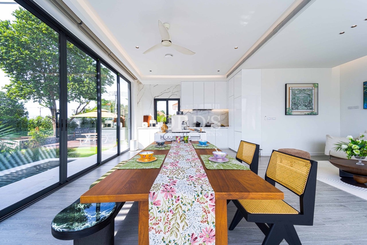 Modern dining table in an open-plan kitchen with floor-to-ceiling glass doors and garden view.