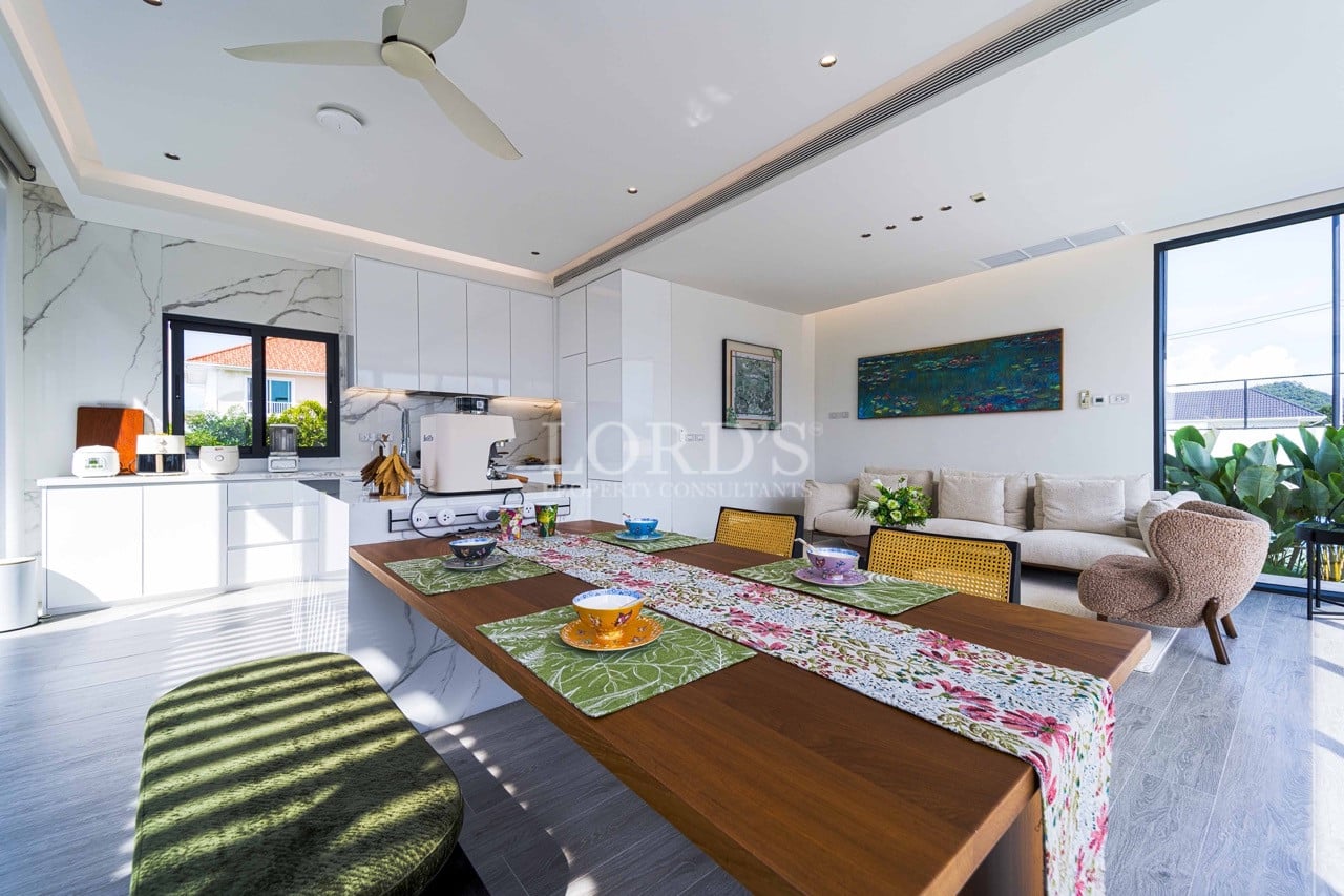 Open-plan kitchen and dining area with wooden table, modern white cabinetry, and bright living room seating.
