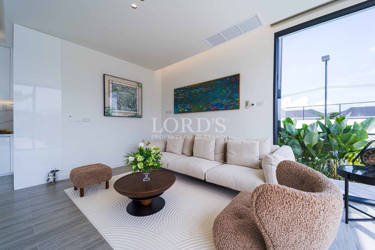 Modern living room with beige sofa, textured lounge chairs, round coffee table, and floor-to-ceiling glass door.