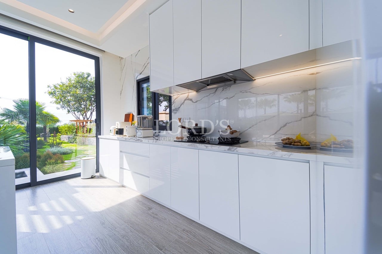 Modern white kitchen with marble backsplash, built-in appliances, and large glass doors opening to a garden.