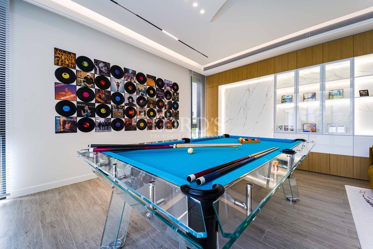 Modern entertainment room with a glass pool table, blue felt surface, vinyl record wall art, and built-in display cabinets.
