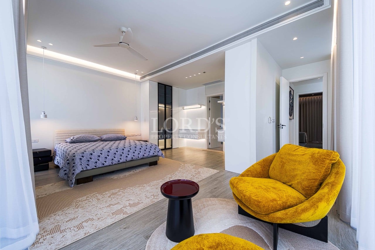 Modern luxury bedroom with open layout, walk-in wardrobe, soft LED lighting, wooden flooring, and a stylish lounge chair.