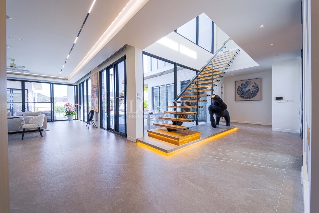 Modern open-plan living area with floating wooden staircase, glass railings, skylight, and floor-to-ceiling windows.